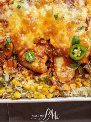 A rectangular baking dish holds a cheesy enchilada casserole with rice, corn, chicken, and sliced jalapeños. Perfect for impressing the in-laws, this stress-free recipe is garnished with fresh cilantro and displayed on a light-colored surface.
