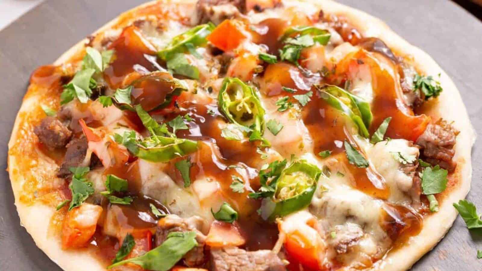 Mexican steak pizza on a round dark wooden board.