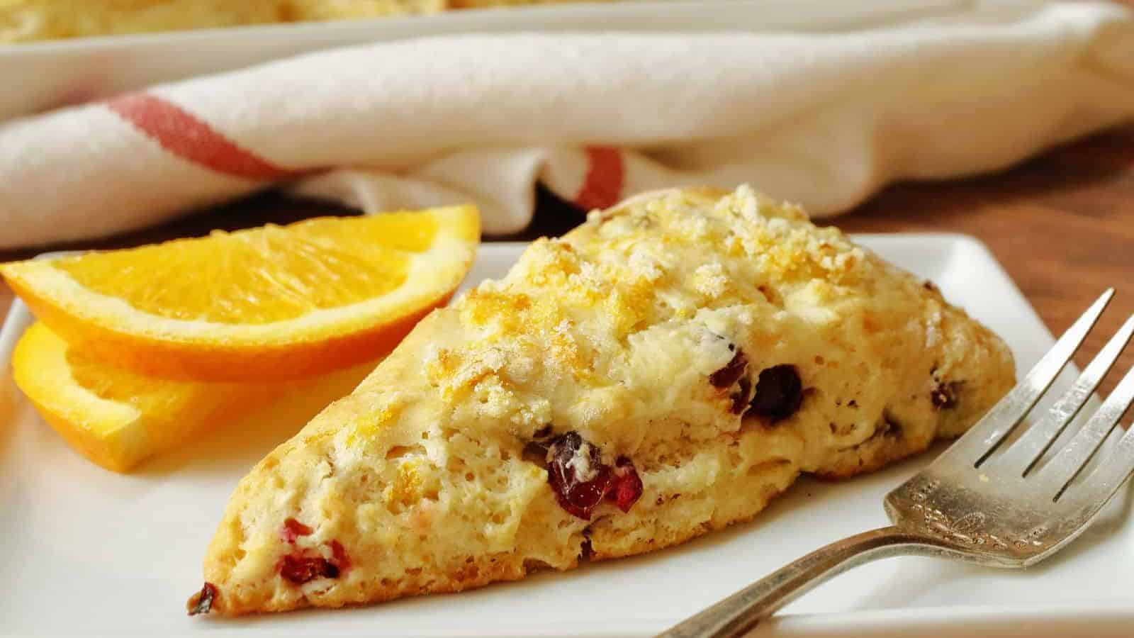 An orange cranberry scones on a white plate with a fork.