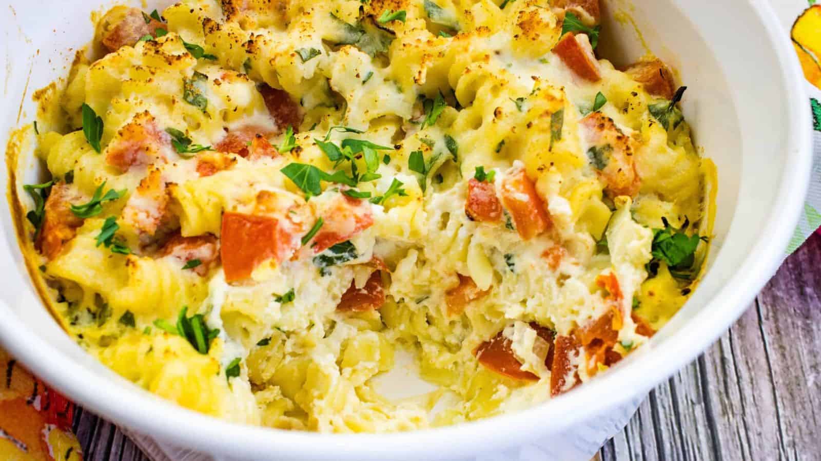 A baked pasta casserole with curly noodles, melted cheese, and fresh herbs makes for one of the best dinner ideas&mdash;perfect for anyone looking to enjoy comfort food while sticking to a food budget. A portion is scooped out to reveal the creamy, cheesy interior.