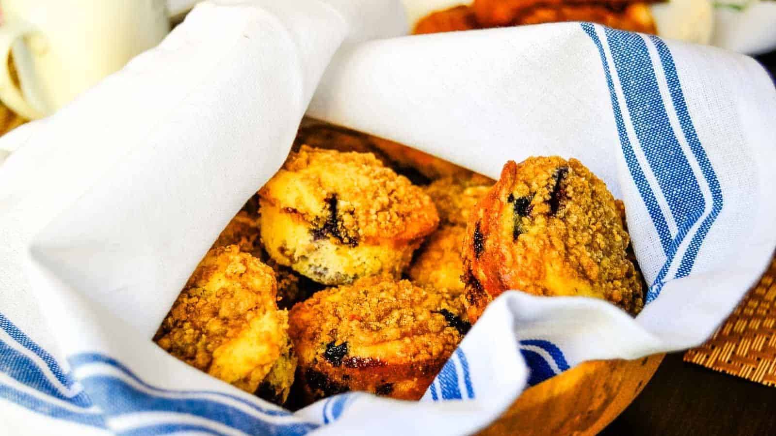 Blueberry muffins in a basket, wrapped in a white and blue towel.