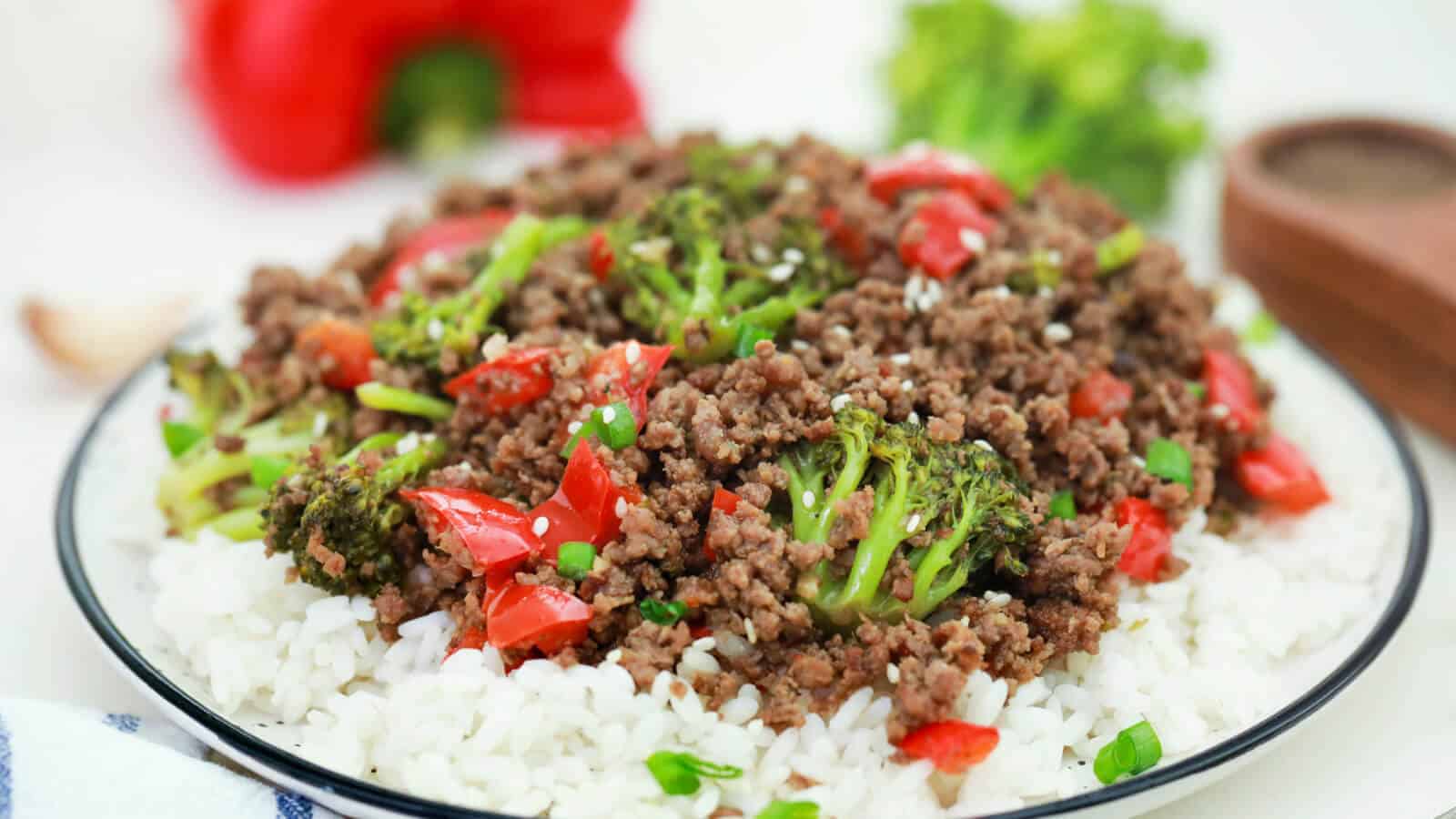 A plate of white rice topped with ground beef, broccoli florets, and chopped red bell peppers, garnished with sesame seeds and green onions&mdash;perfect for quick dinner ideas or to add to your list of main dishes.