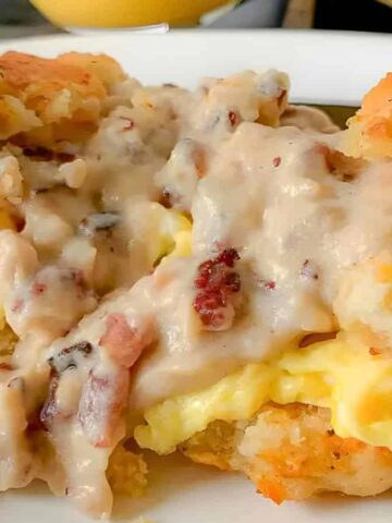 A close-up of two biscuit halves topped with scrambled eggs and creamy sausage gravy, served on a white plate.
