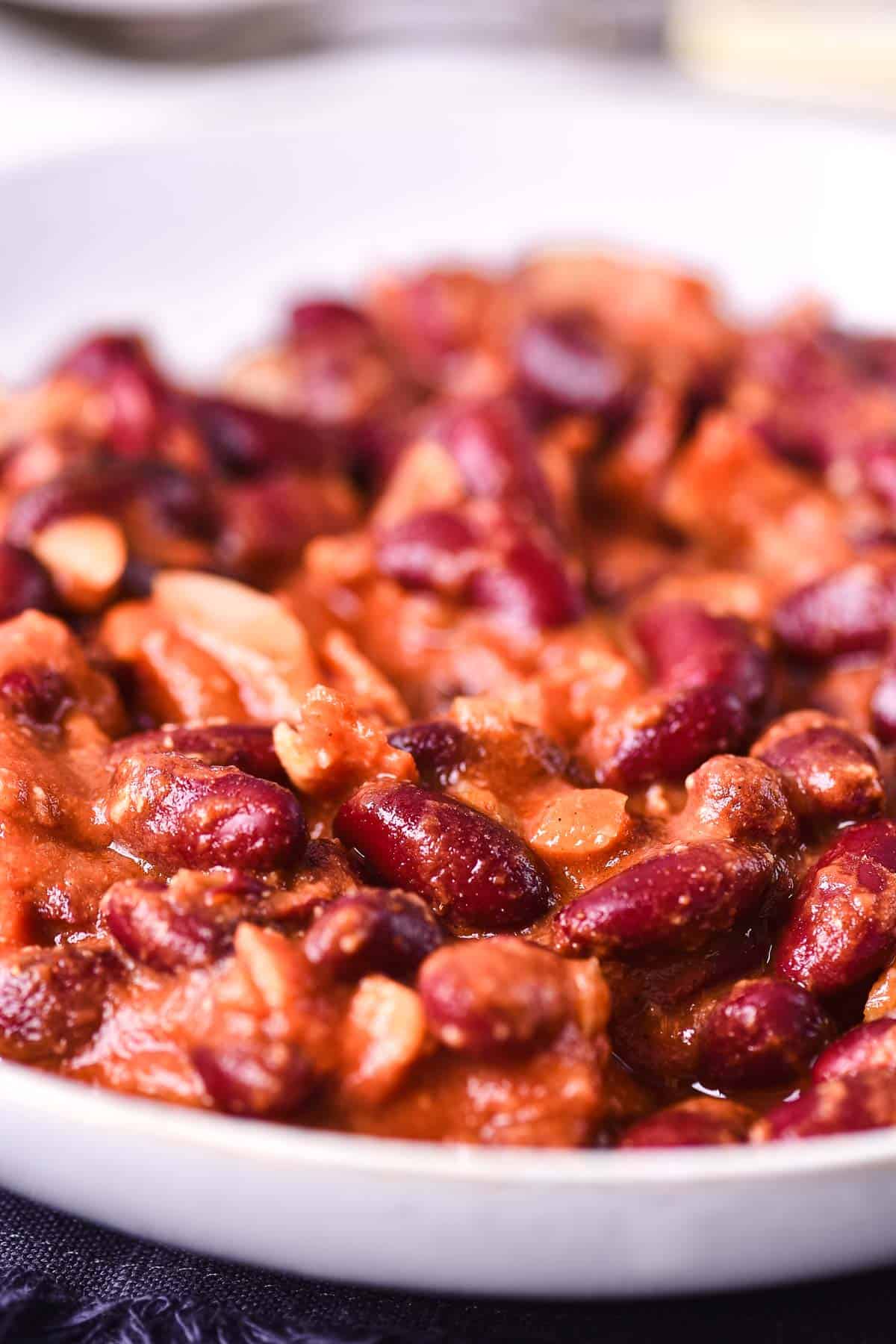 A close-up of a bowl filled with red kidney beans, chopped onions, and a thick tomato-based sauce, reminiscent of Slow Cooker Baked Beans or a hearty chili stew.