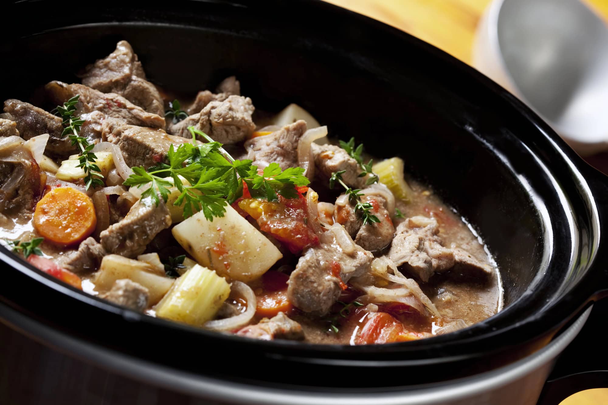 A close-up of a slow cooker filled with beef stew, including chunks of beef, carrots, potatoes, celery, and garnished with fresh parsley&mdash;an inviting dish perfect for trying out new slow cooker tips.