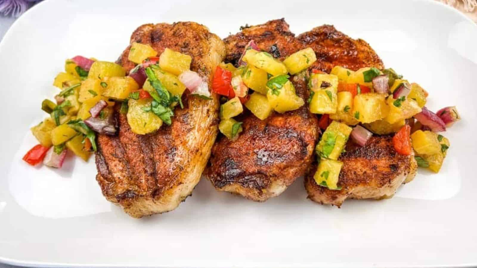 Grilled pork chops with pineapple salsa on a white plate.