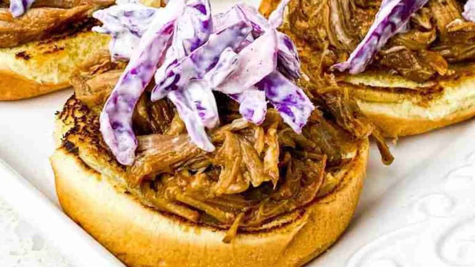 Open-faced sandwich with pulled pork and purple coleslaw on a toasted bun.