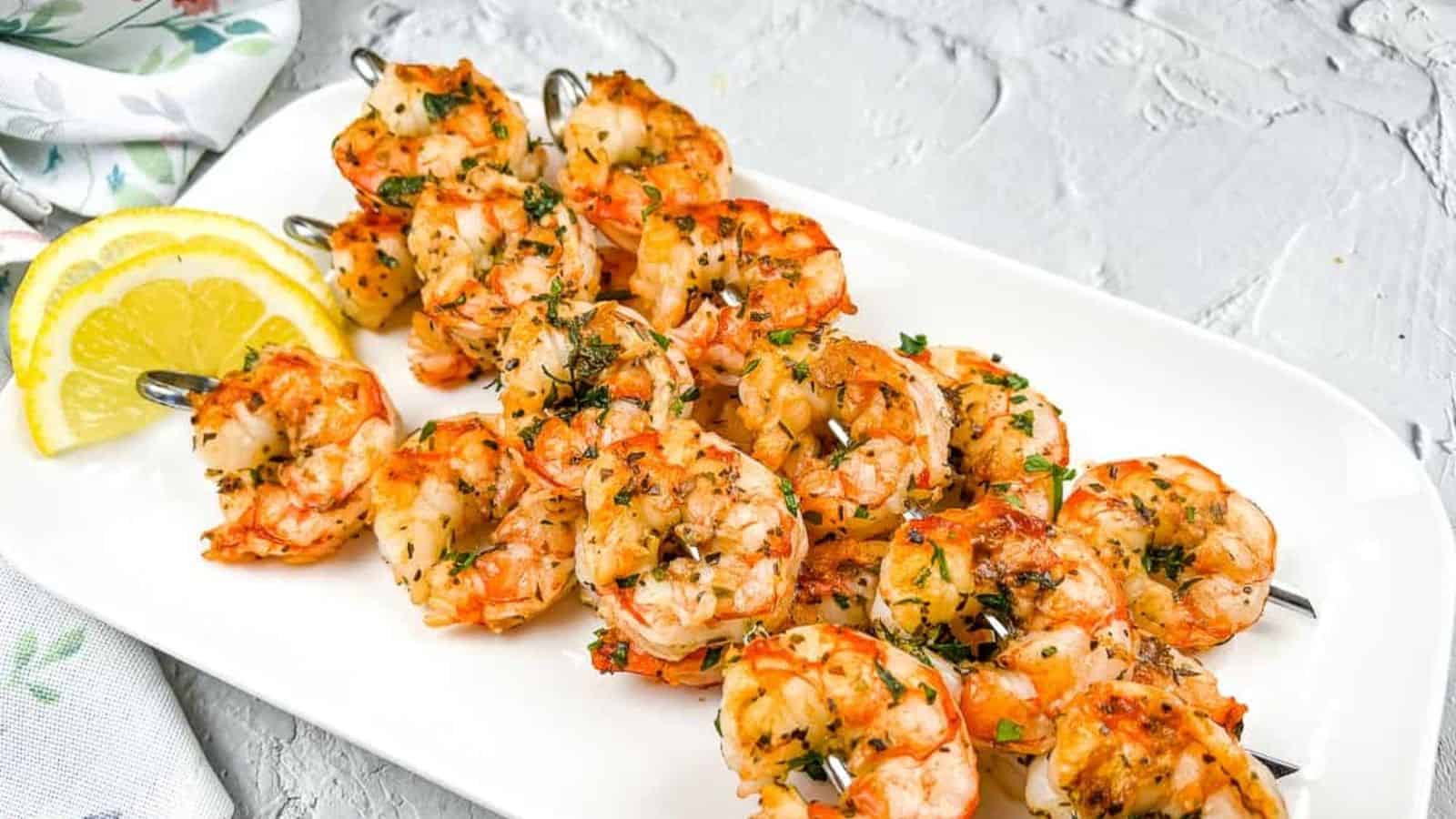 Shrimp skewers on a white plate with lemon wedges.