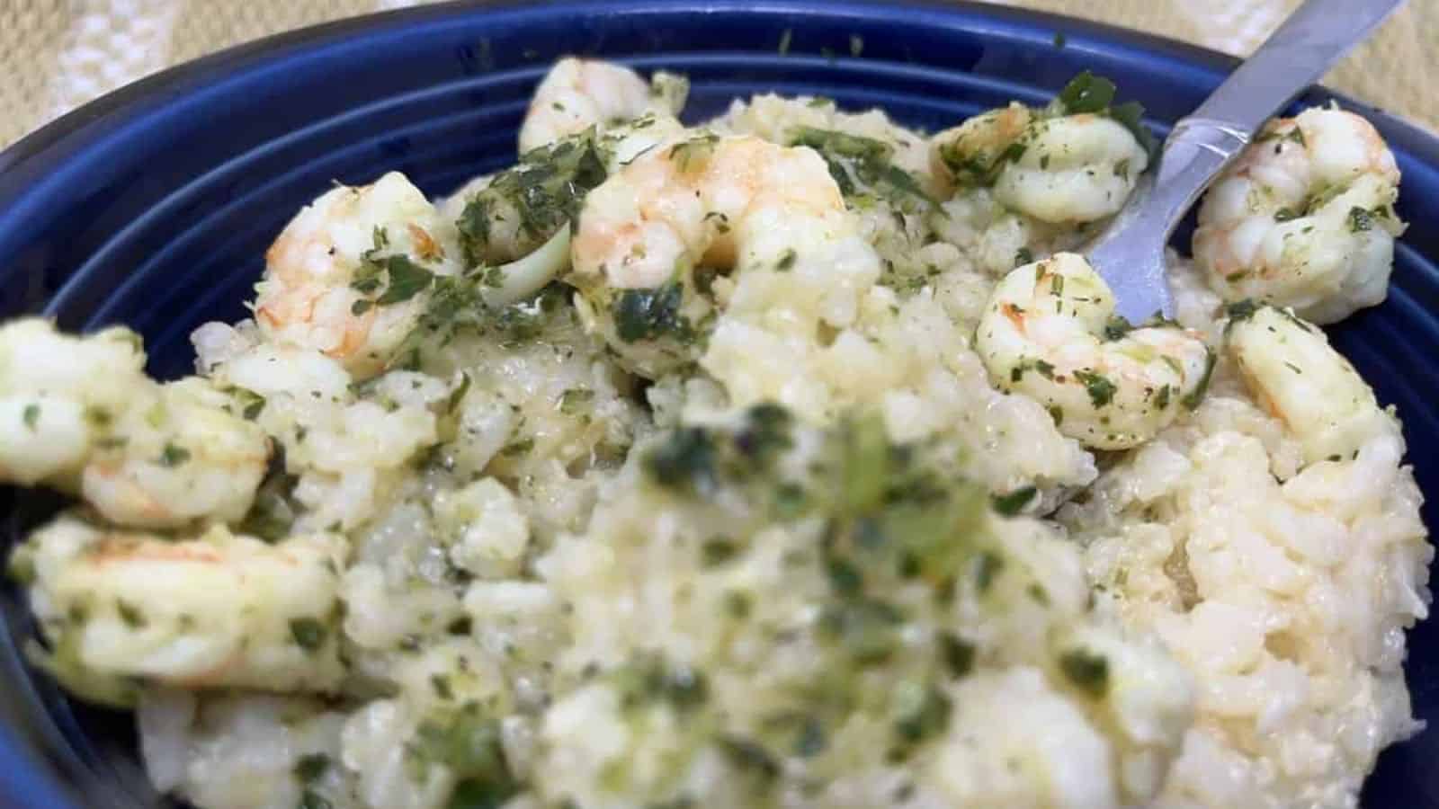 A bowl of creamy risotto with shrimp, topped with green herbs, and a spoon resting on the side.