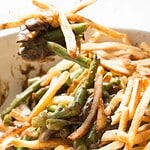 A close-up of French fries mixed with green beans and mushrooms coated in a brown sauce, with one forkful being lifted from this unique twist on a Green Bean Casserole Recipe.