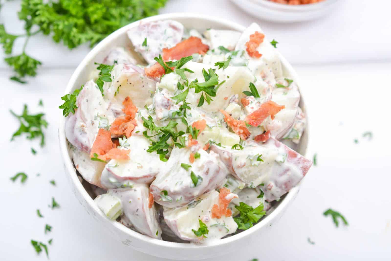 Red potato salad in bowl with bacon and parsley garnish.