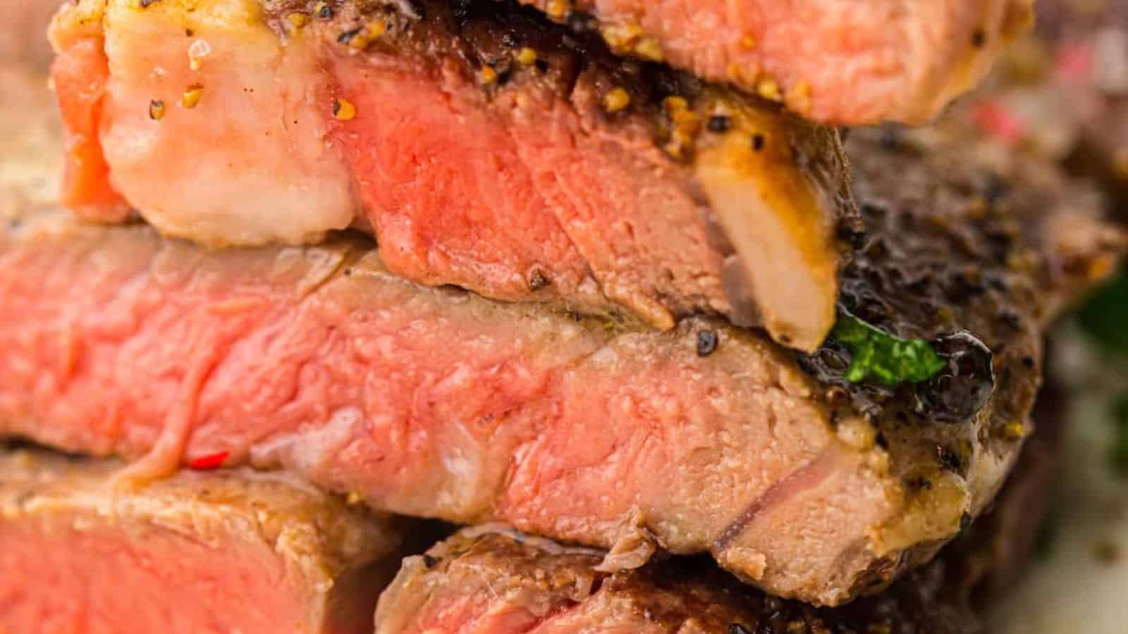Close-up of a stack of medium-rare, seasoned steak slices, showcasing a pink and juicy interior with a seared crust.