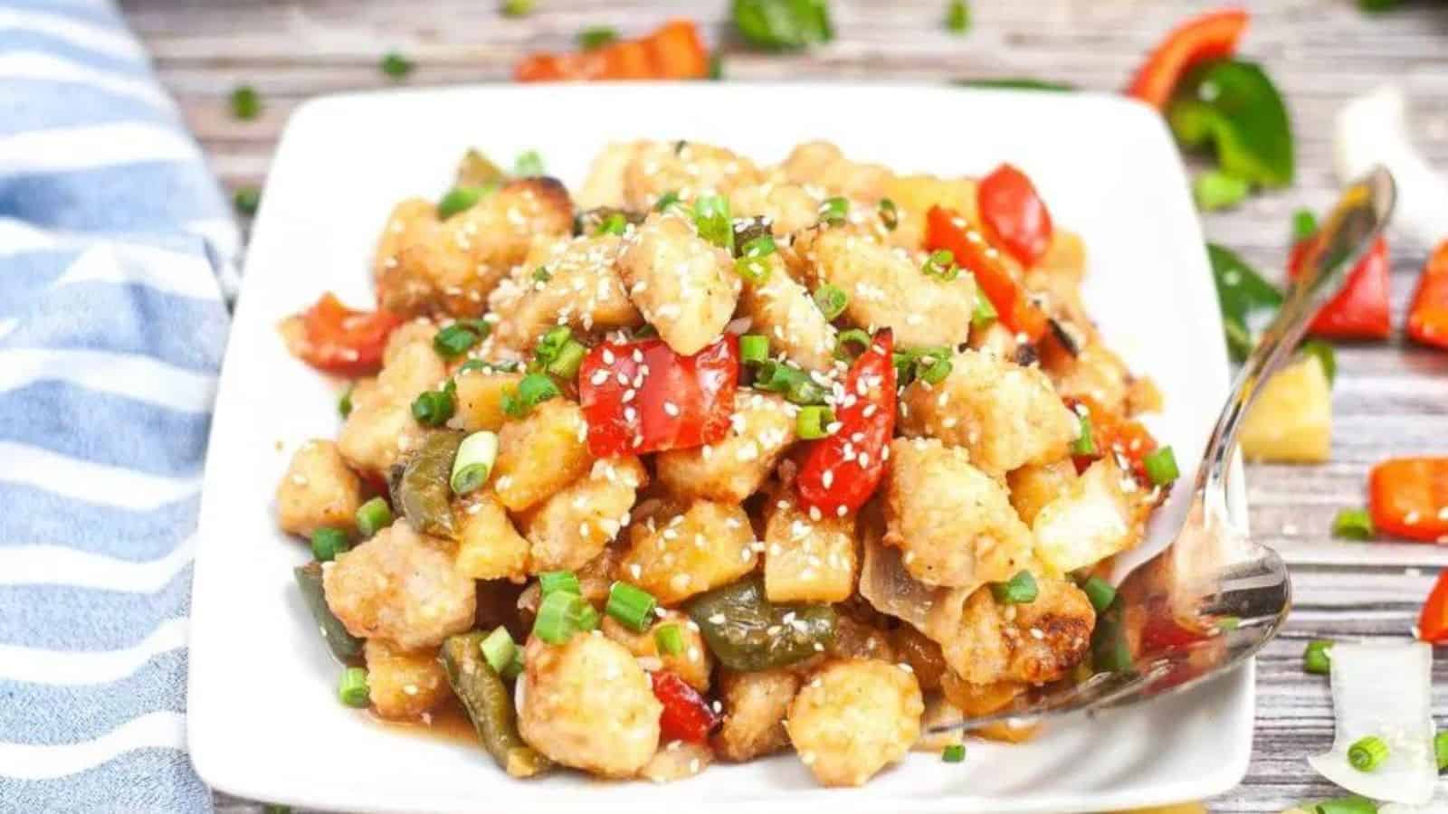 Sweet and sour chicken chunks in a glossy sauce, served on a white plate with garnish.