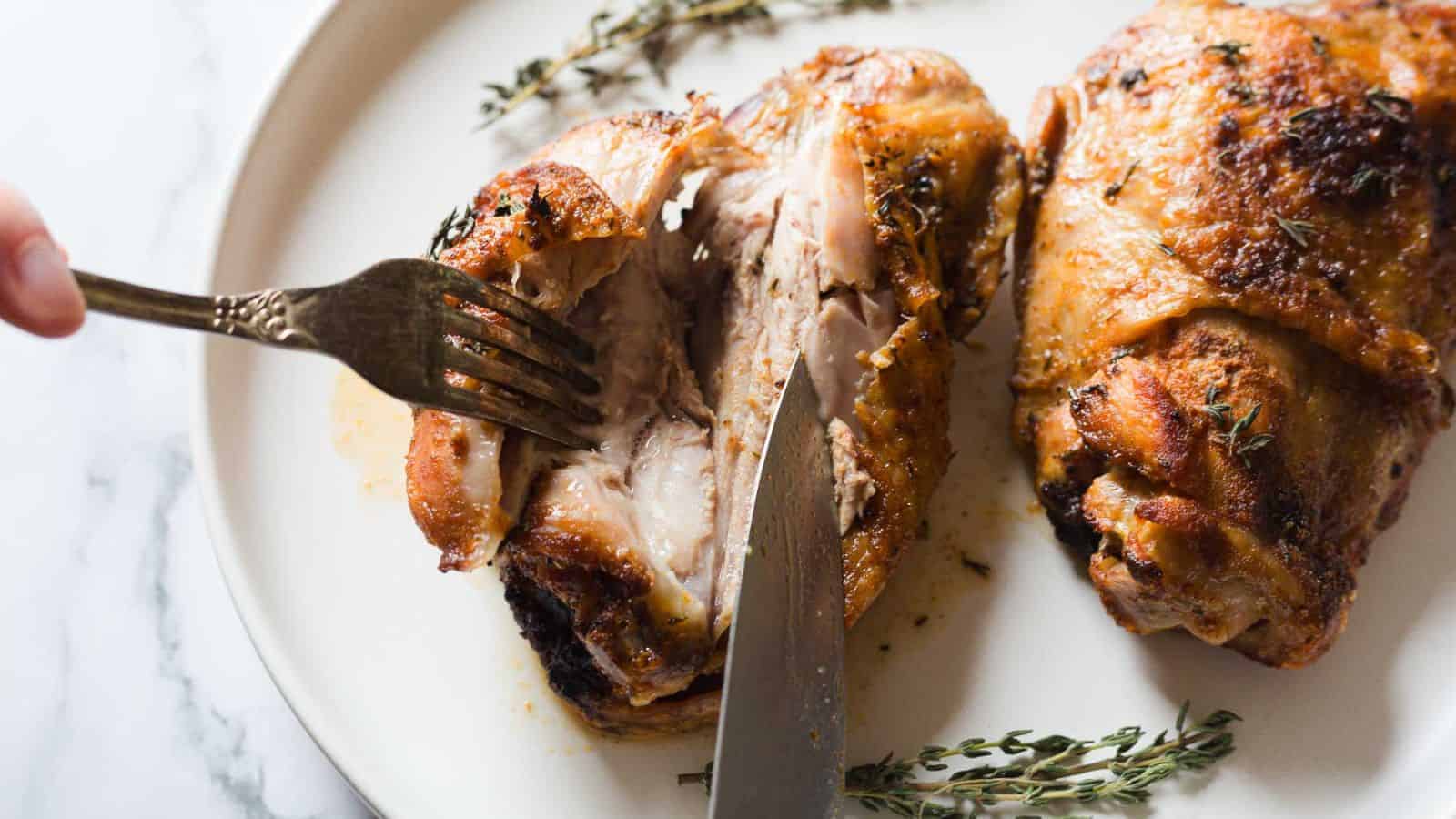 Two roasted chicken thighs on a white plate garnished with sprigs of thyme. A ceramic jar is partially visible in the background on the left.