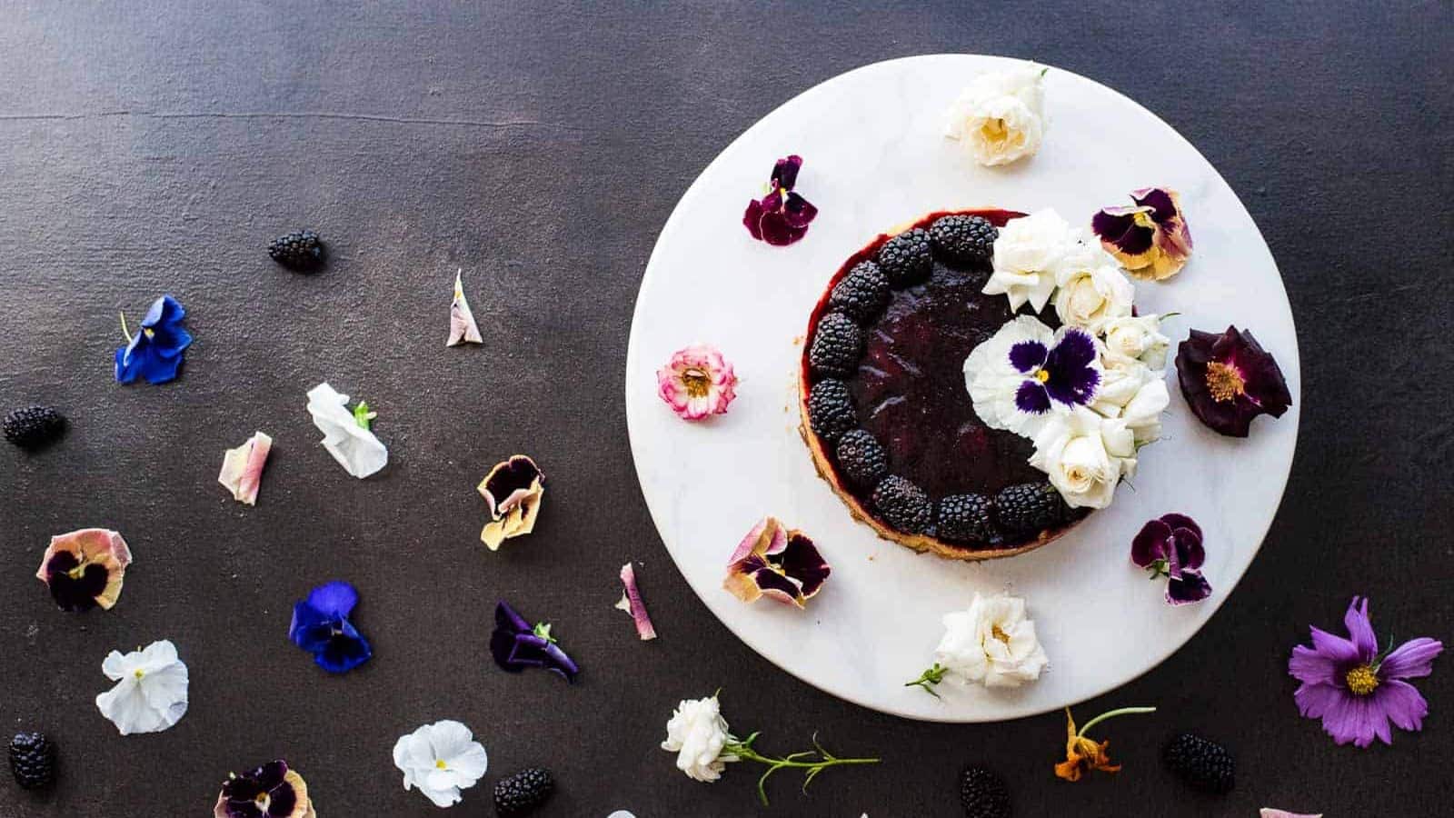 Overhead shot of a blackberry lime tart on a white plate surrounded by edible flowers.