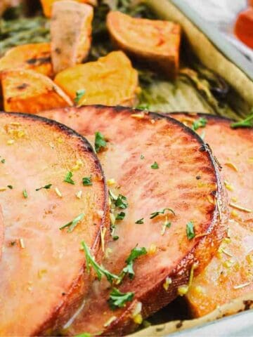 Sliced ham and roasted sweet potatoes on a baking sheet, garnished with herbs—perfect for easy and flavorful dinners.