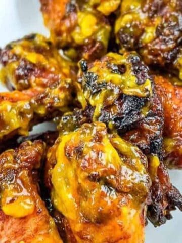 A close-up of several cooked chicken wings coated in a yellow-orange sauce, served on a white rectangular plate. The wings have a glazed and slightly charred appearance.