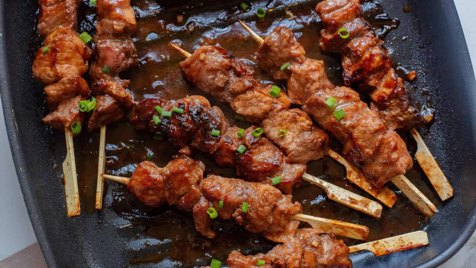 Hoisin Pork Tenderloin on skewers in a pan.