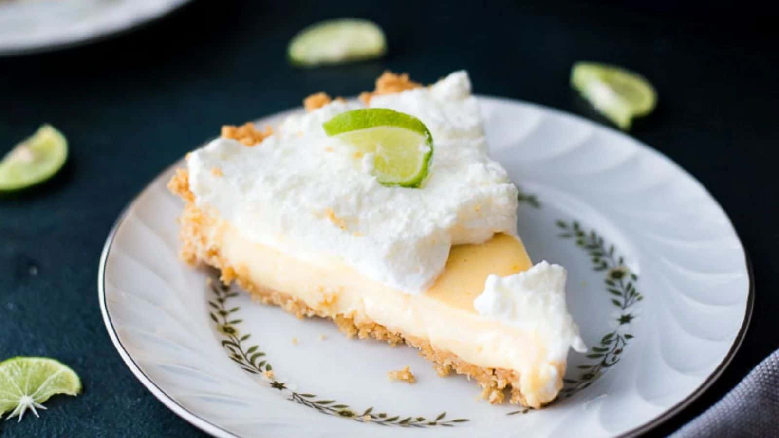 Key lime pie with a graham cracker crust, topped with coconut whipped cream and garnished with lime slices.