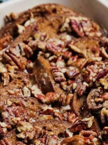 A baking dish filled with slices of bread topped with chopped pecans, all coated in a brown sauce, suggesting a baked French toast casserole.