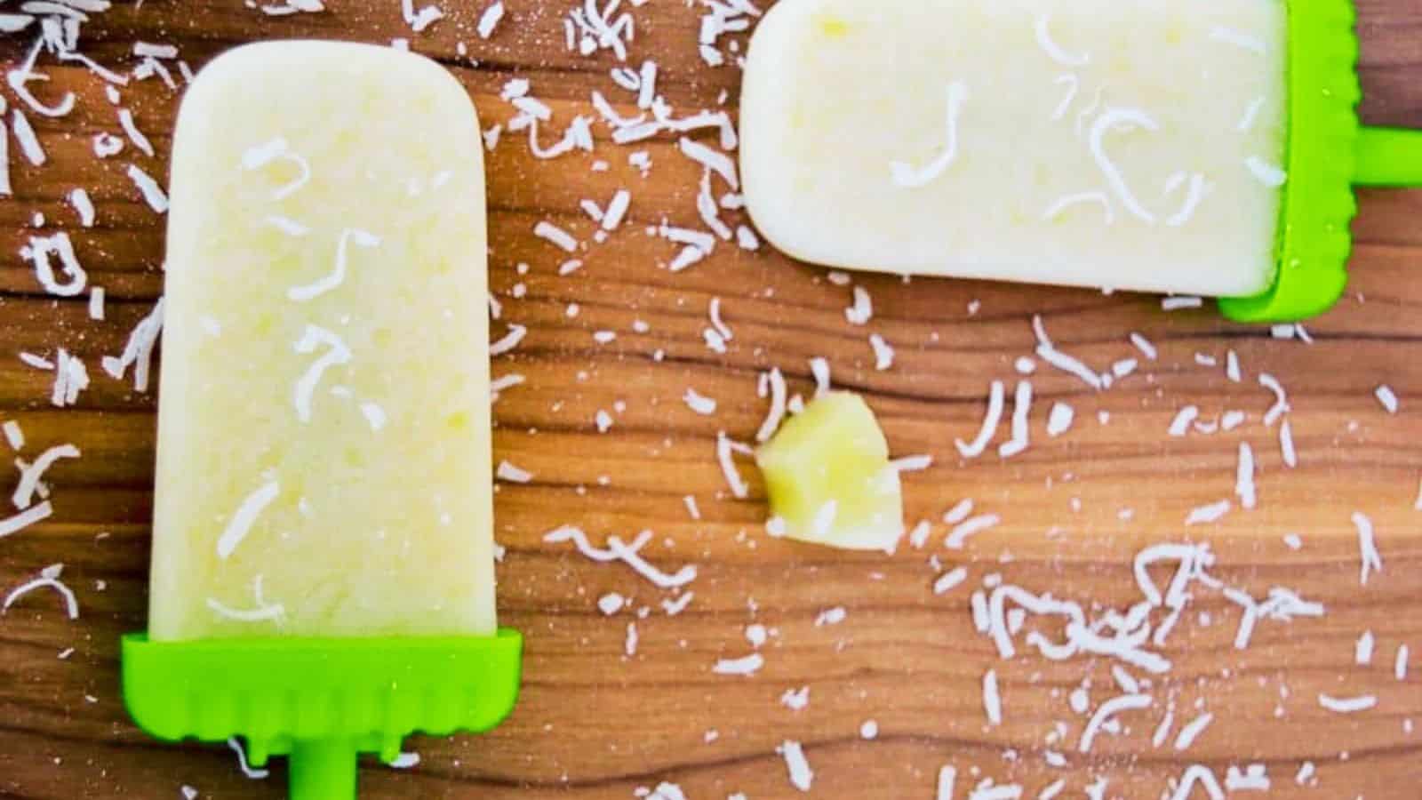 Two pina colada popsicles on a wooden background.