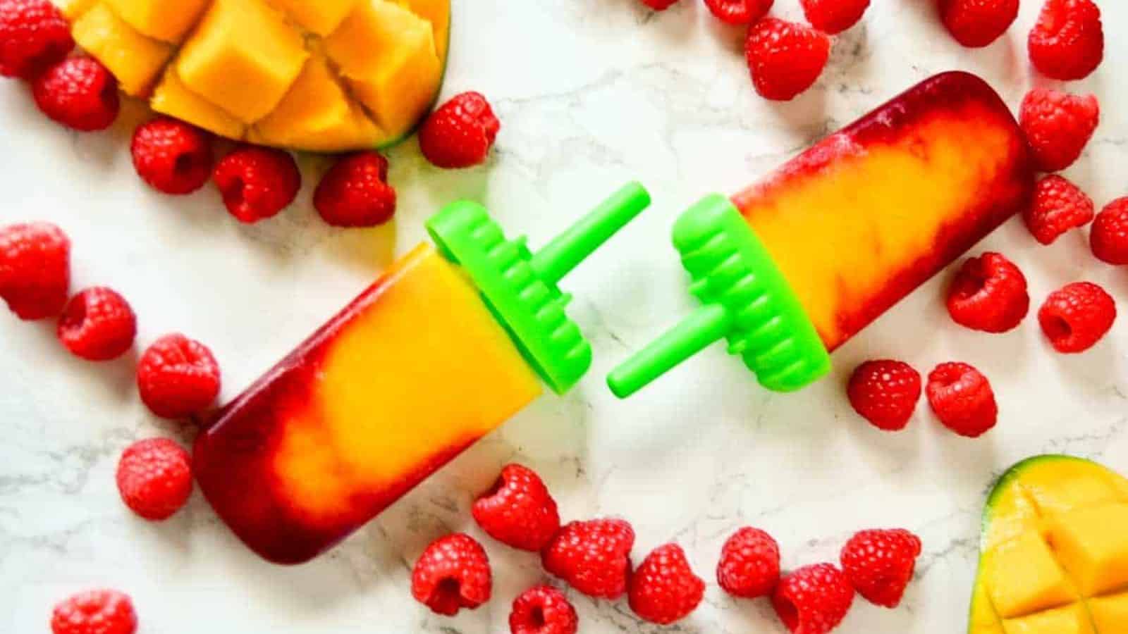 Raspberry mango popsicle on a marble background next to raspberries and mango.
