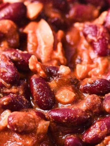 A close-up of a dish containing red kidney beans in a thick, reddish-brown sauce with visible pieces of onion.
