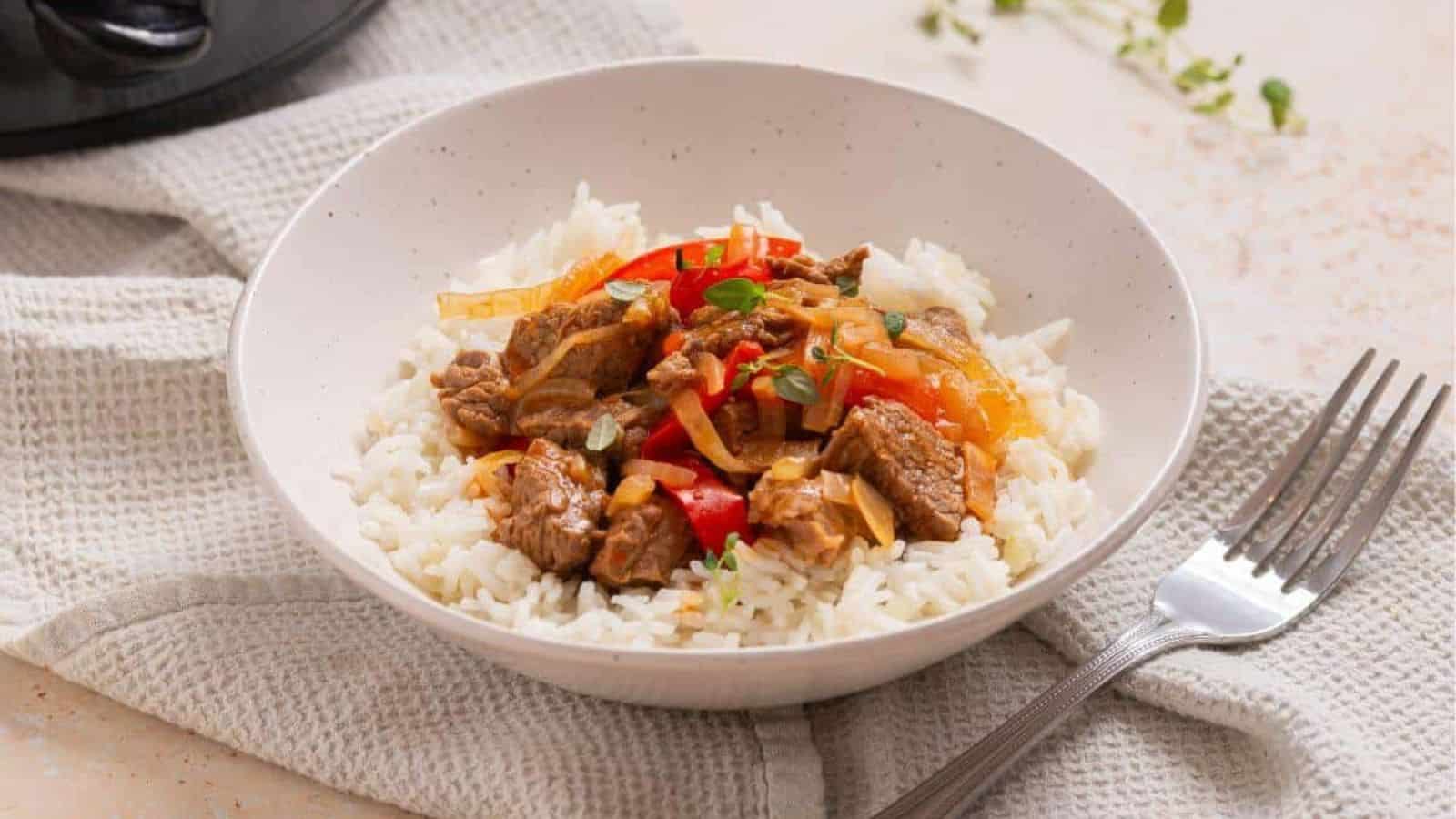 A bowl of rice with meat and peppers in front of a slow cooker.