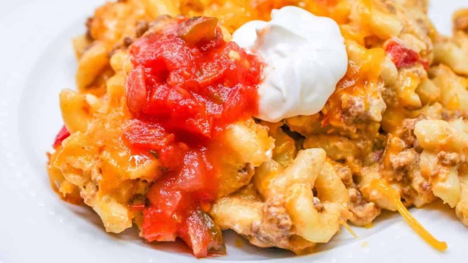 A plate of cheesy pasta with ground meat, topped with tomato sauce and a dollop of sour cream.