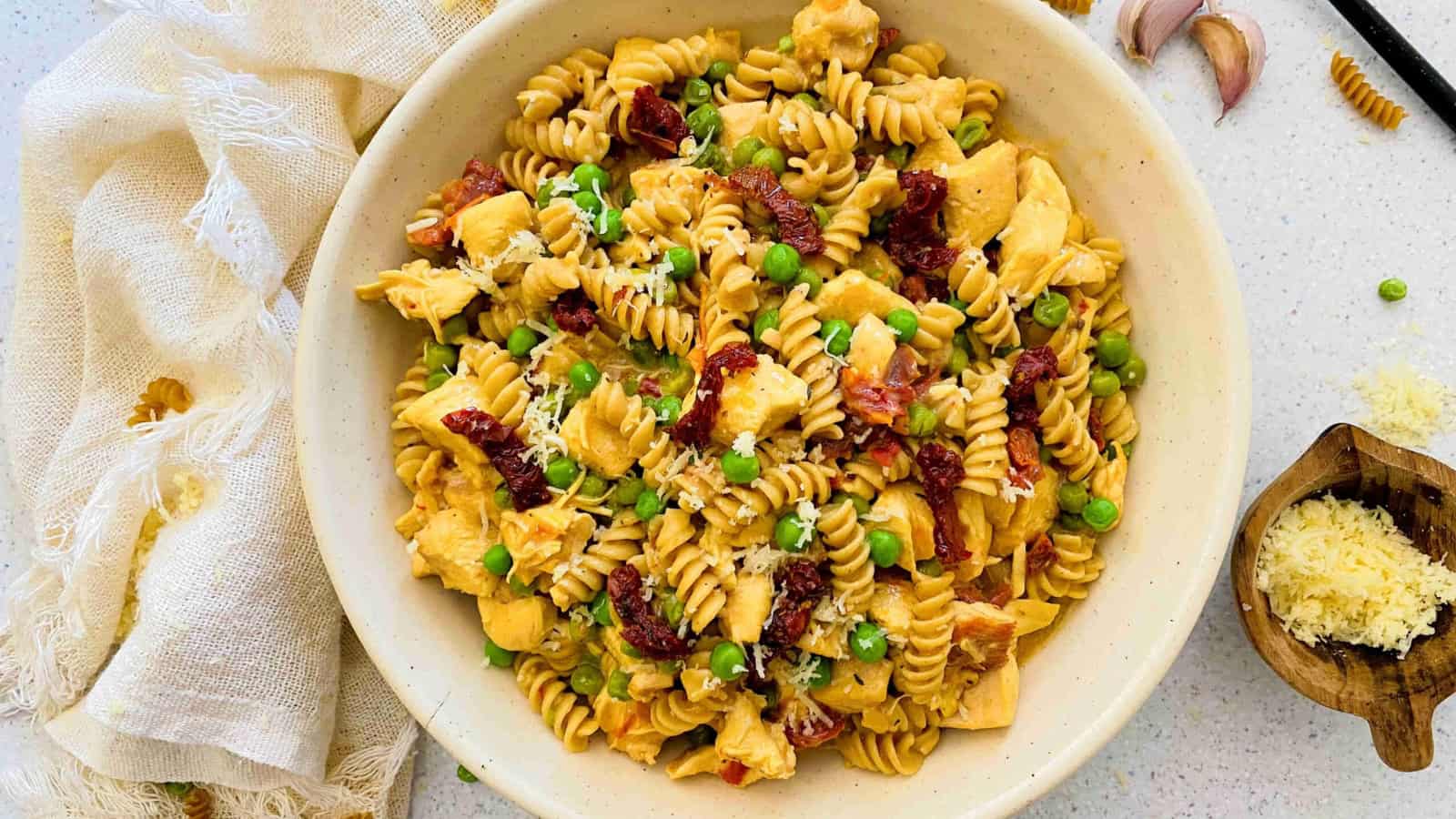 white bowl with chicken pasta with sundried tomatoes and peas and garlic and a light linen around the bowl.