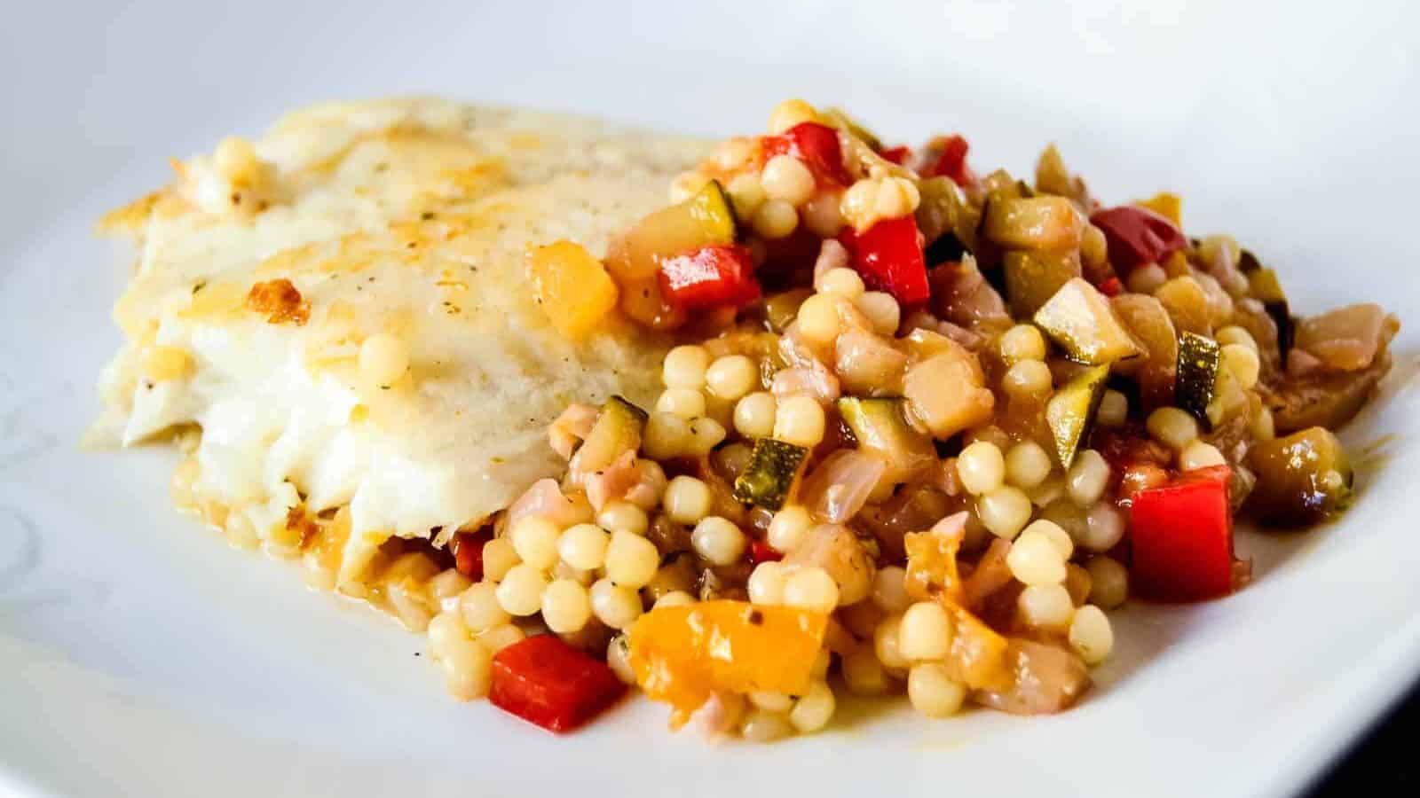 Summer veggie couscous with sauteed tilapia served on a white plate.