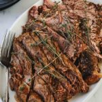A white oval plate with sliced and shredded pot roast beef garnished with fresh thyme sprigs, placed on a marble surface next to a fork and an Instant Pot—perfect for showcasing your favorite easy brisket recipe.