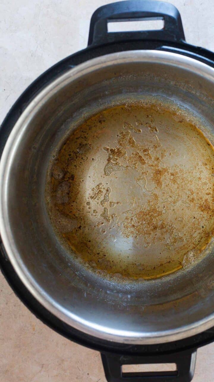 A close-up view of the inside of a stainless steel pot, possibly after making Instant Pot Gravy, with brown residue and stains on the bottom. The pot, featuring black handles on each side, rests on a light surface.