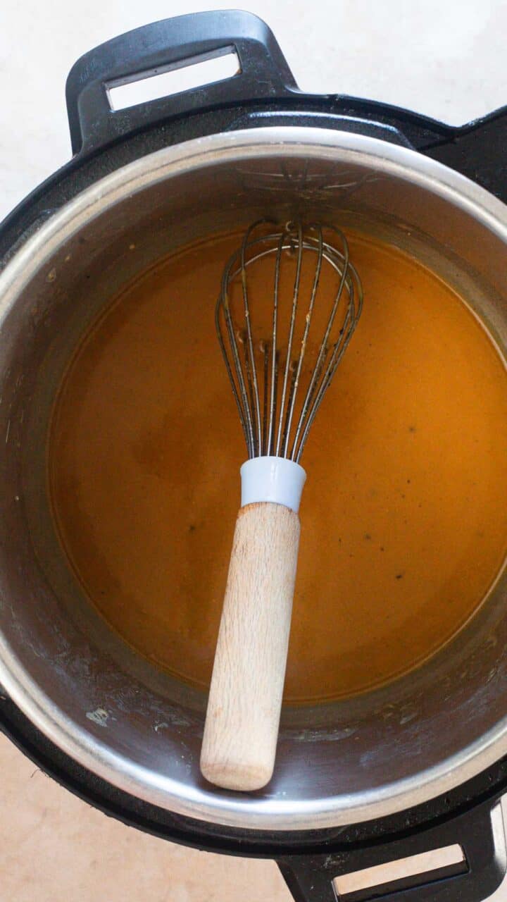 A metal whisk with a wooden handle rests inside a pot containing a smooth, orange-brown liquid, likely an Easy Gravy Recipe or sauce, viewed from above.