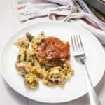 A white plate holds a serving of Chicken Pot Pie with a golden-brown biscuit topping and creamy vegetable filling, inspired by a classic Pillsbury casserole recipe. A fork rests on the plate, with a towel in the background.
