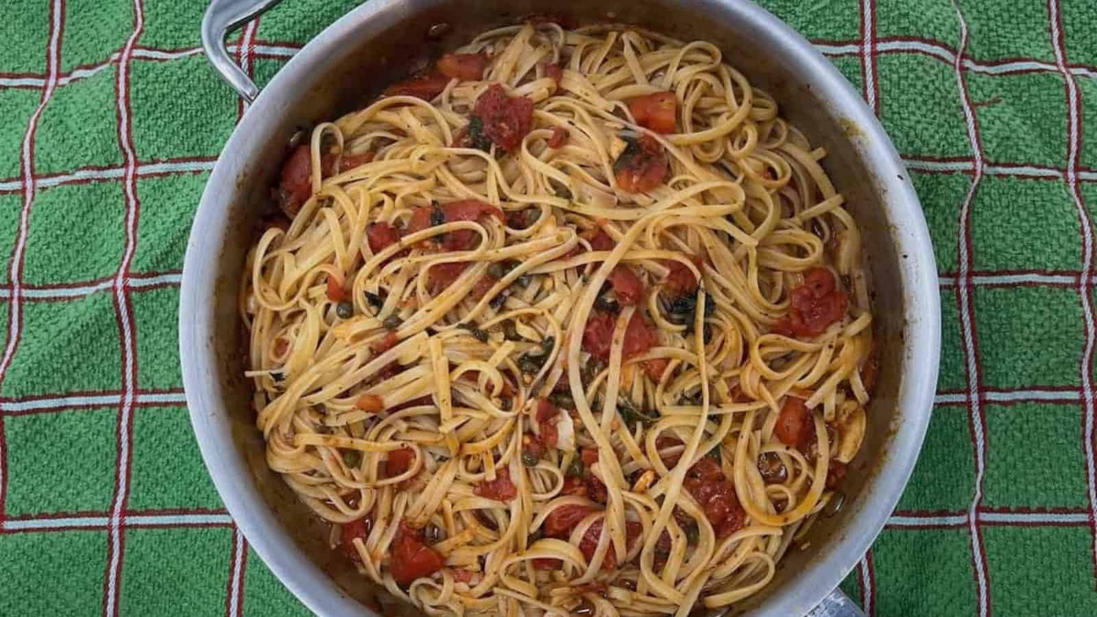 A pan full of spaghetti and tomatoes on a tablecloth.