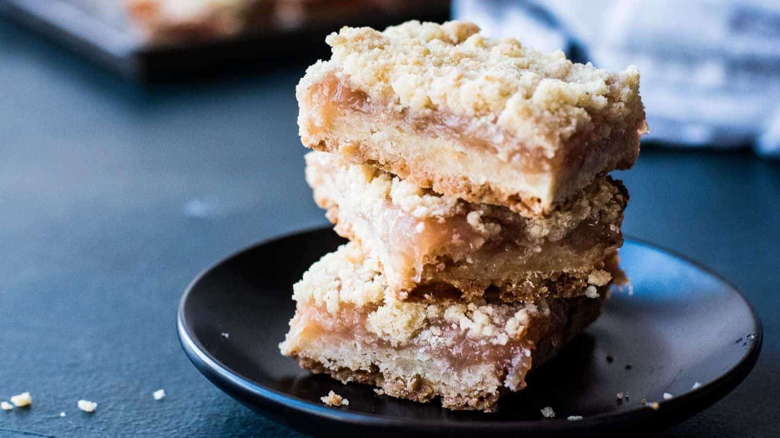 A stack of three peach crumble bars on a black plate.