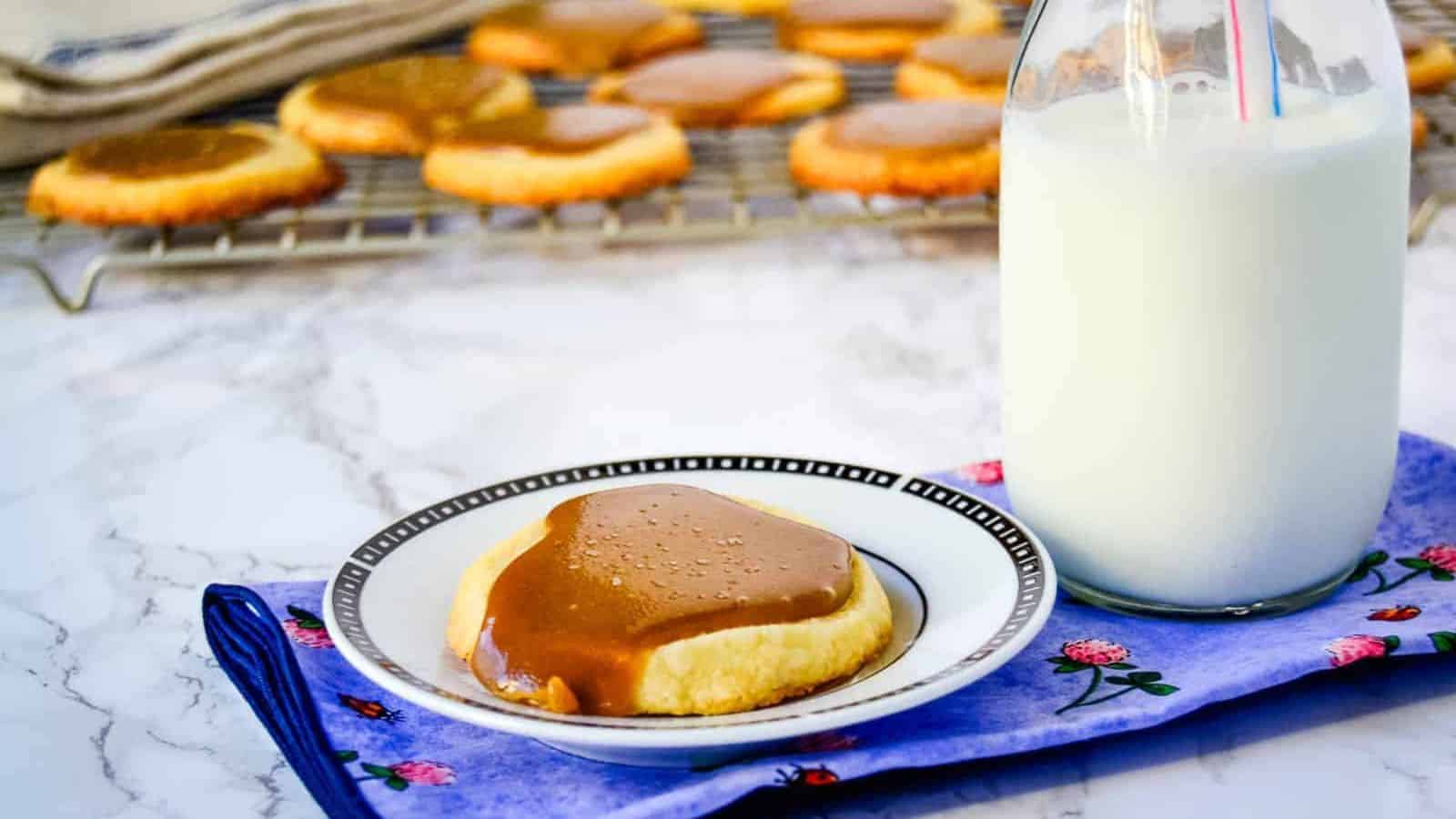 One Salted Bourbon Caramel Shortbread Cookies cookie on a white plate next to a bottle of milk.