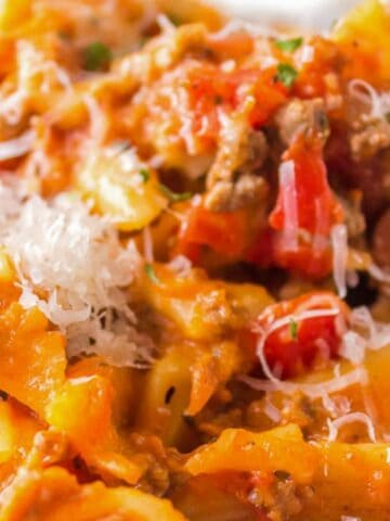 A close-up of baked ziti pasta with tomato sauce, ground meat, and melted cheese, topped with grated parmesan, served on a white plate.