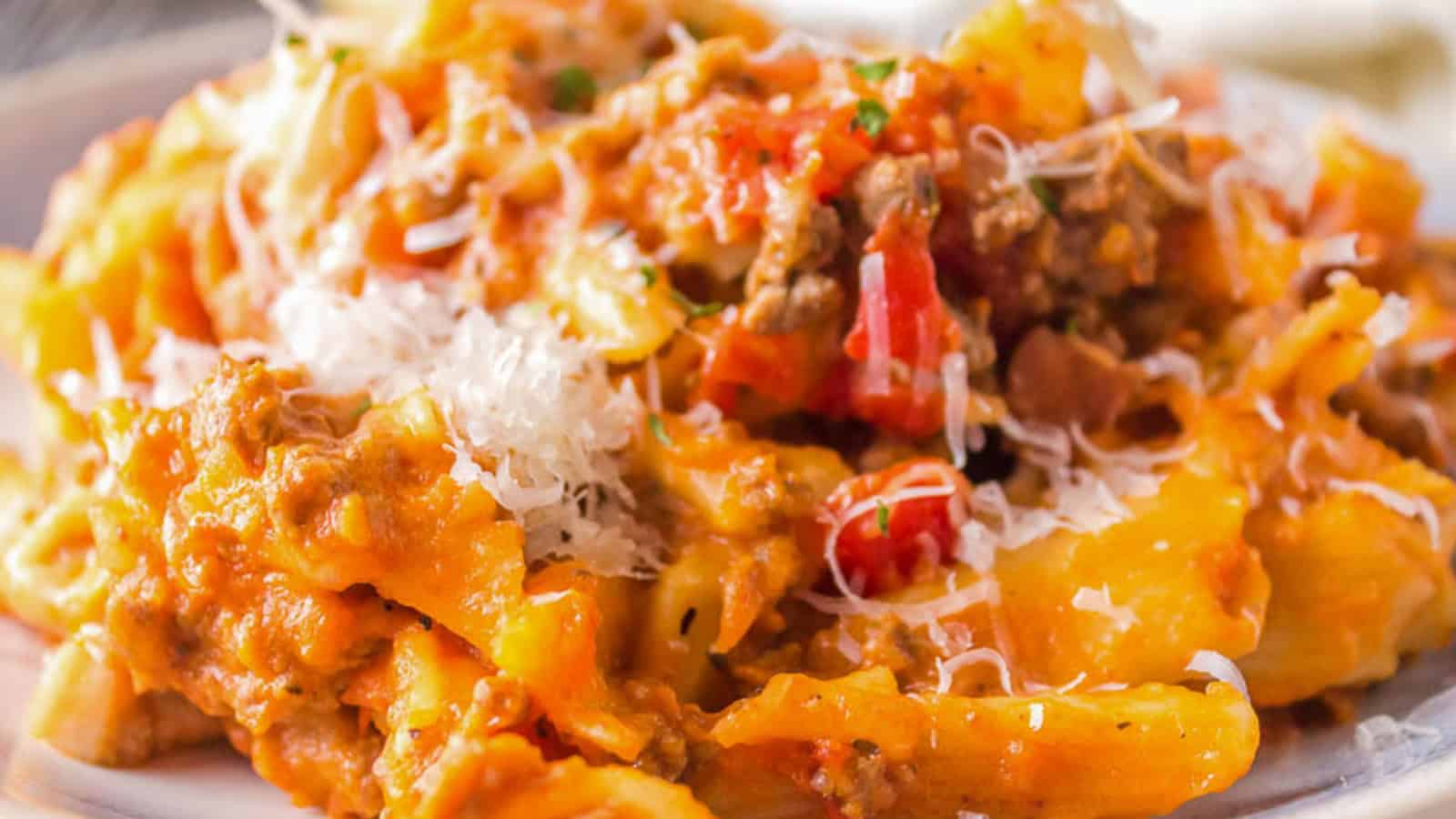 A close-up of baked ziti pasta with tomato sauce, ground meat, and melted cheese, topped with grated parmesan, served on a white plate.