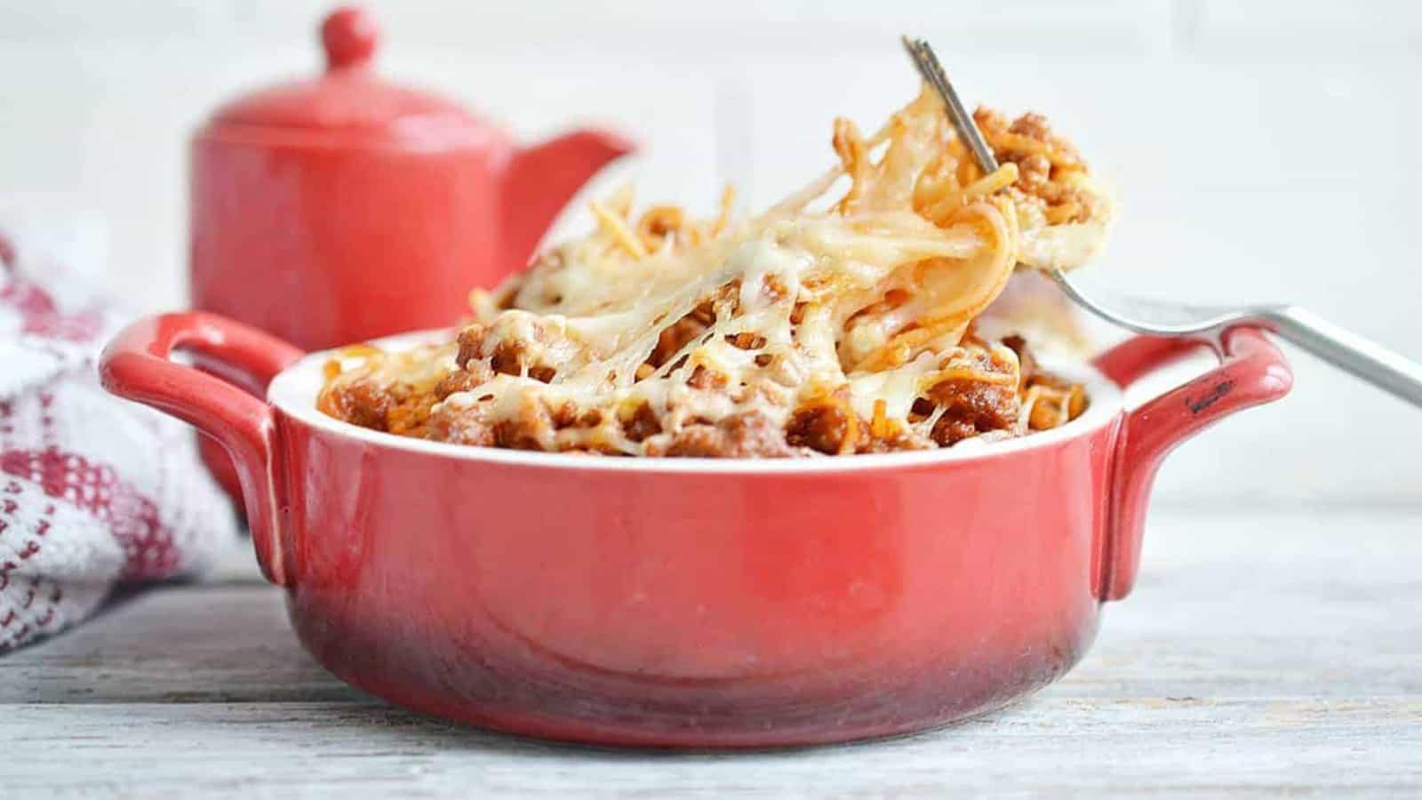 A red dish of spaghetti casserole with a fork in it, to the side.