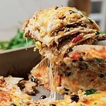 A cheesy slice of make ahead turkey burrito casserole is being lifted from a baking dish, with layers of tortilla and gooey melted cheese stretching.