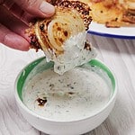 A hand dips a crispy fried onion slice into a bowl of creamy herb dip.