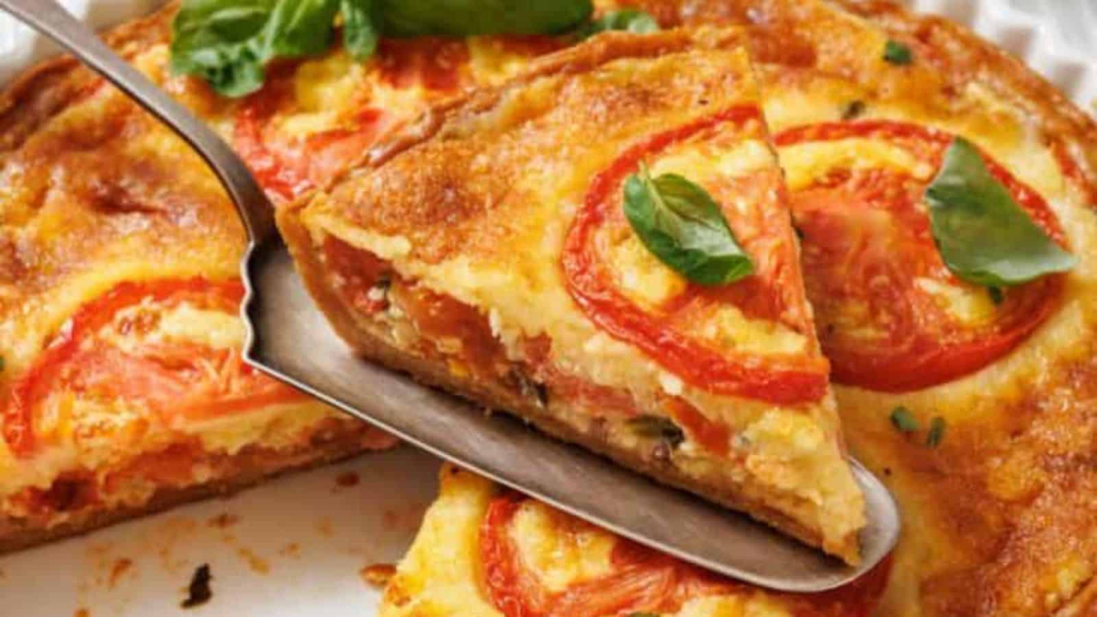A slice of tomato pie on a white plate with a serving utensil, and a whole tomato pie in a white fluted dish, are shown on a marble surface with a small bowl of spices and basil leaves.