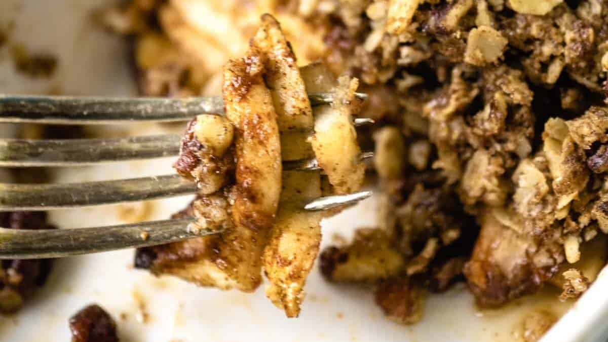 A fork holds spiced apple slices with oat crumble, close-up, with more crumble in the background.