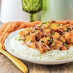 Slow Cooker beef stew with carrots and potatoes served over mashed potatoes on a white plate, garnished with parsley.