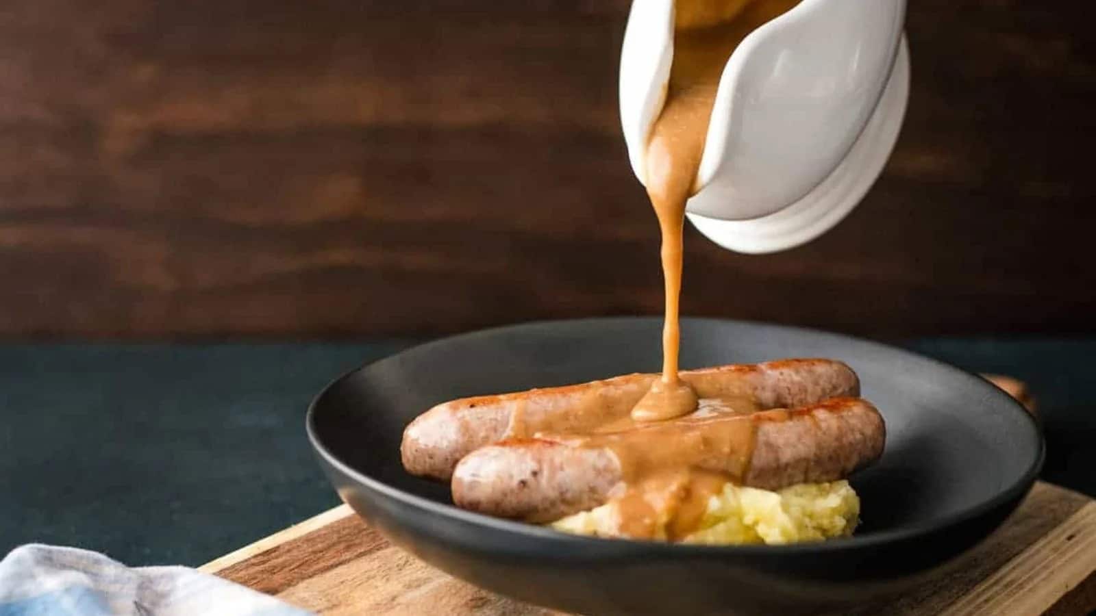 Gravy being poured over sausages and mashed potatoes.