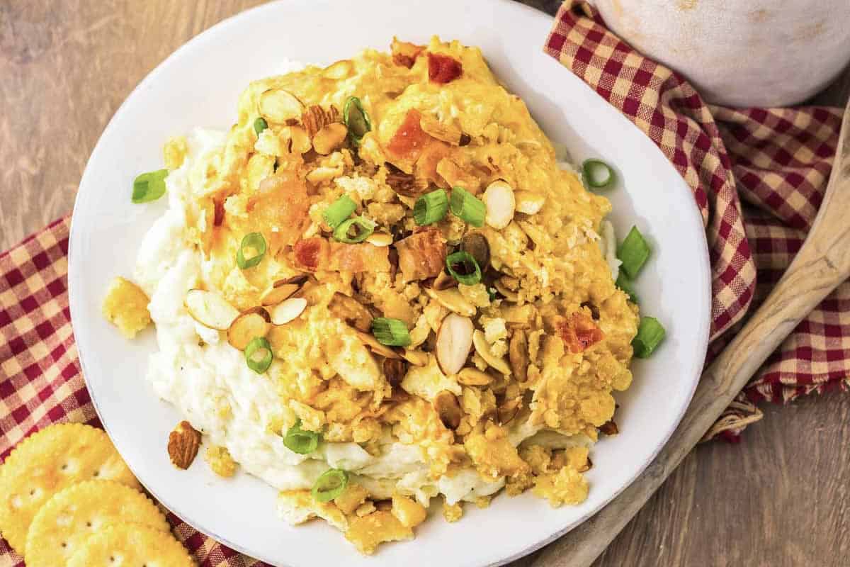A plate of creamy Neiman Marcus Chicken casserole topped with sliced almonds, green onions, and served on a checkered napkin.
