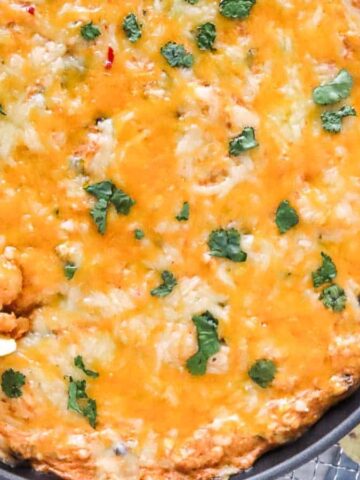 Cheesy baked dip in a skillet topped with cilantro, served with tortilla chips and lime slices on the side.
