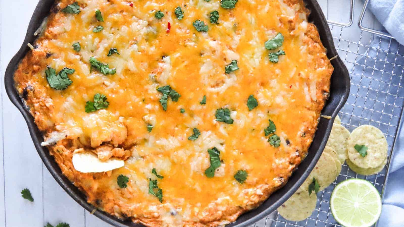 Cheesy baked dip in a skillet topped with cilantro, served with tortilla chips and lime slices on the side.